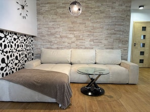 A modern living room with a sofa, a glass coffee table, a patterned wall, and a wooden floor. - Modern Apartment | 2 Balconies | Parking | Close to Metro (Warszawa)
