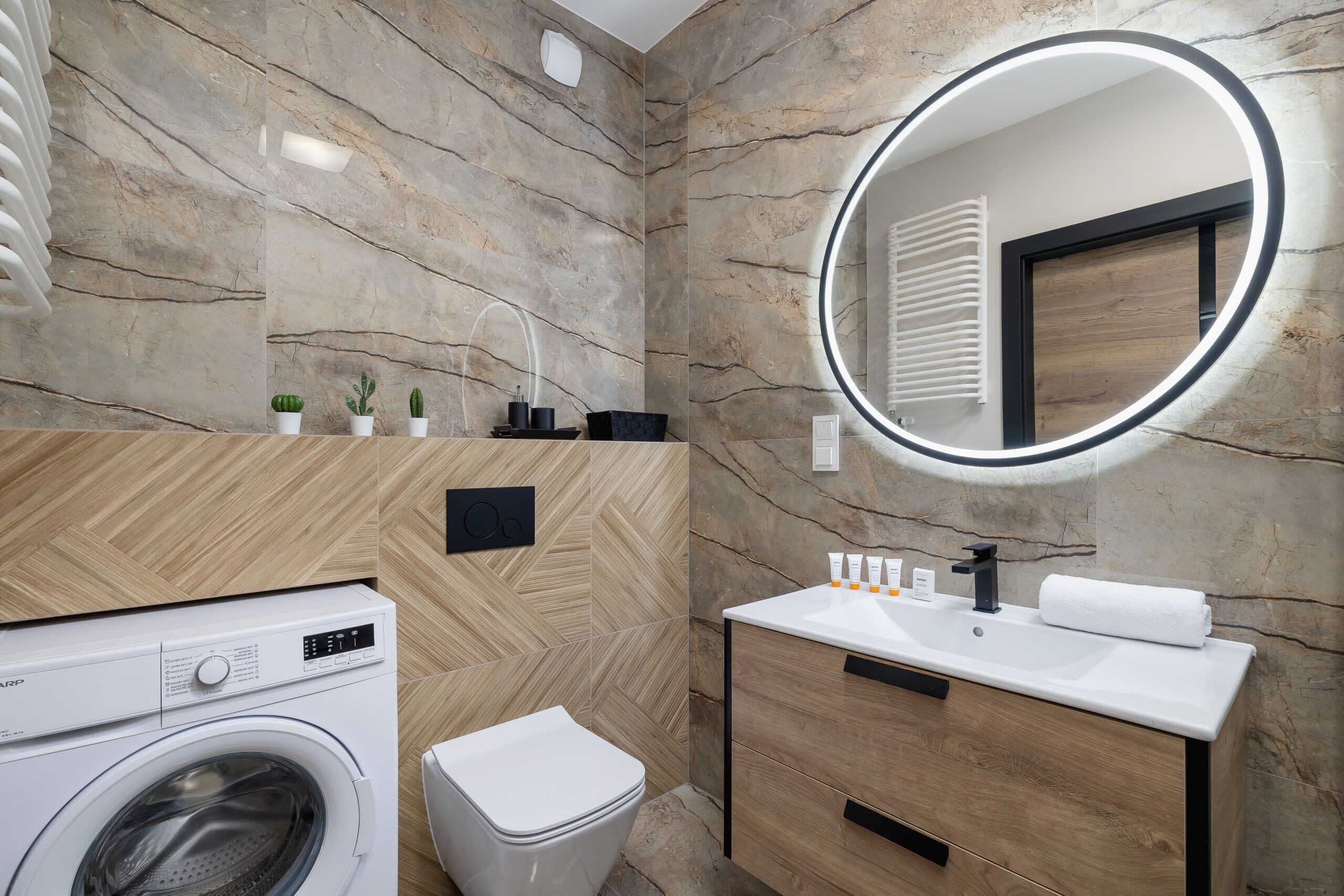 Un baño moderno con lavadora, inodoro, tocador con espejo y pared con patrón de espiga.