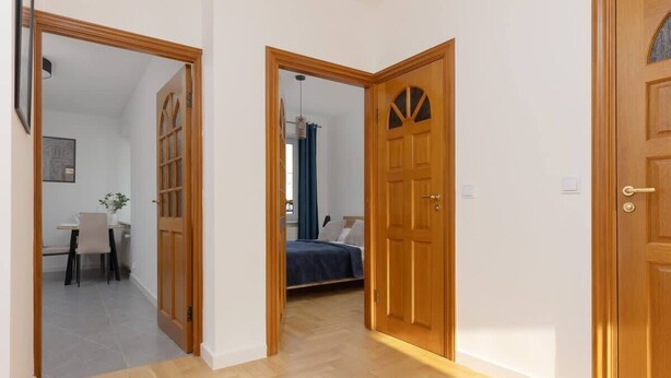 A hallway with wooden doors leading to a bedroom with a bed and a bathroom with a shower curtain.