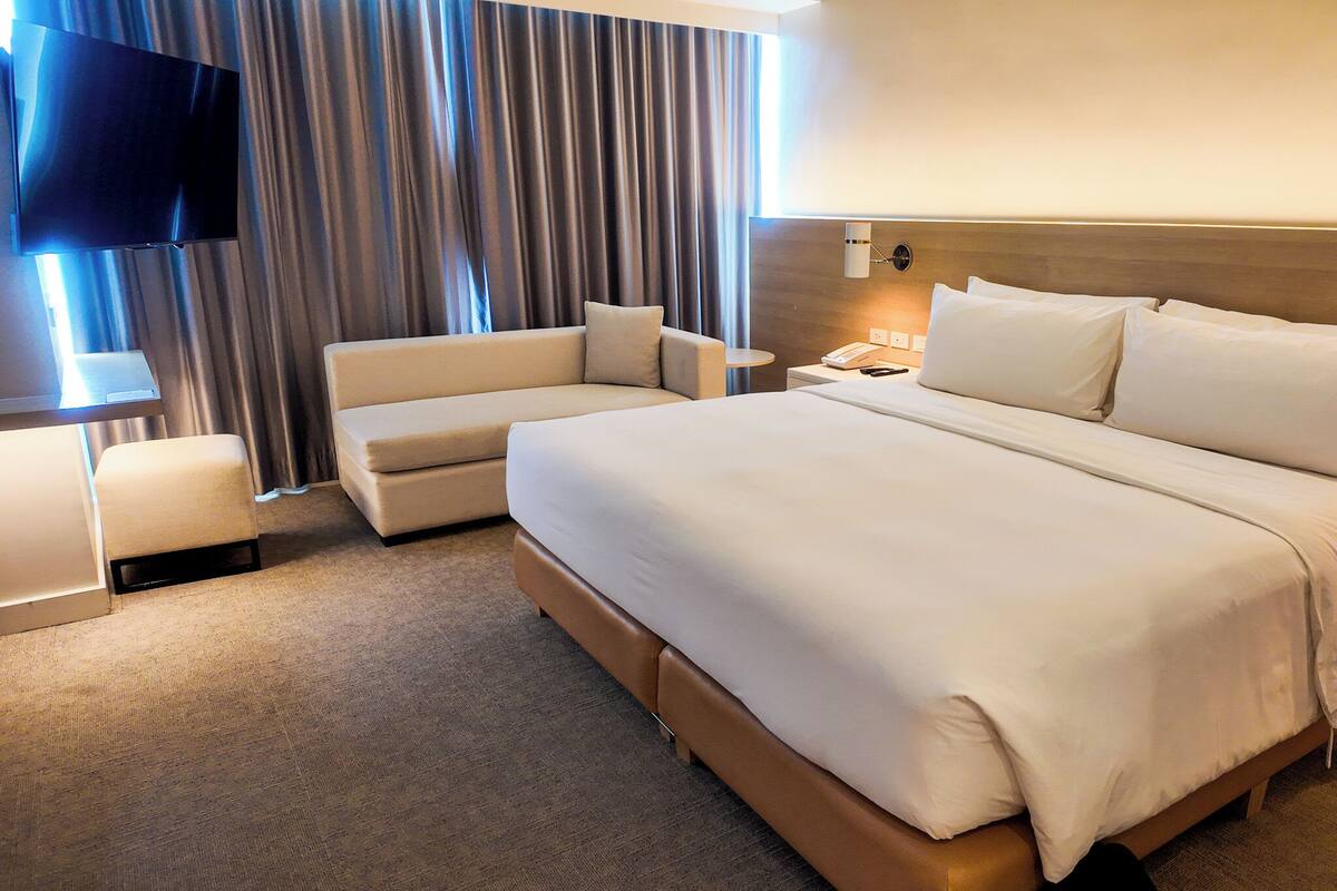 Habitación de hotel con una cama grande, un sofá, un televisor y una mesita de noche.