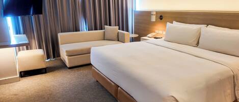 Habitación de hotel con una cama grande, un sofá, un televisor y una mesita de noche.
