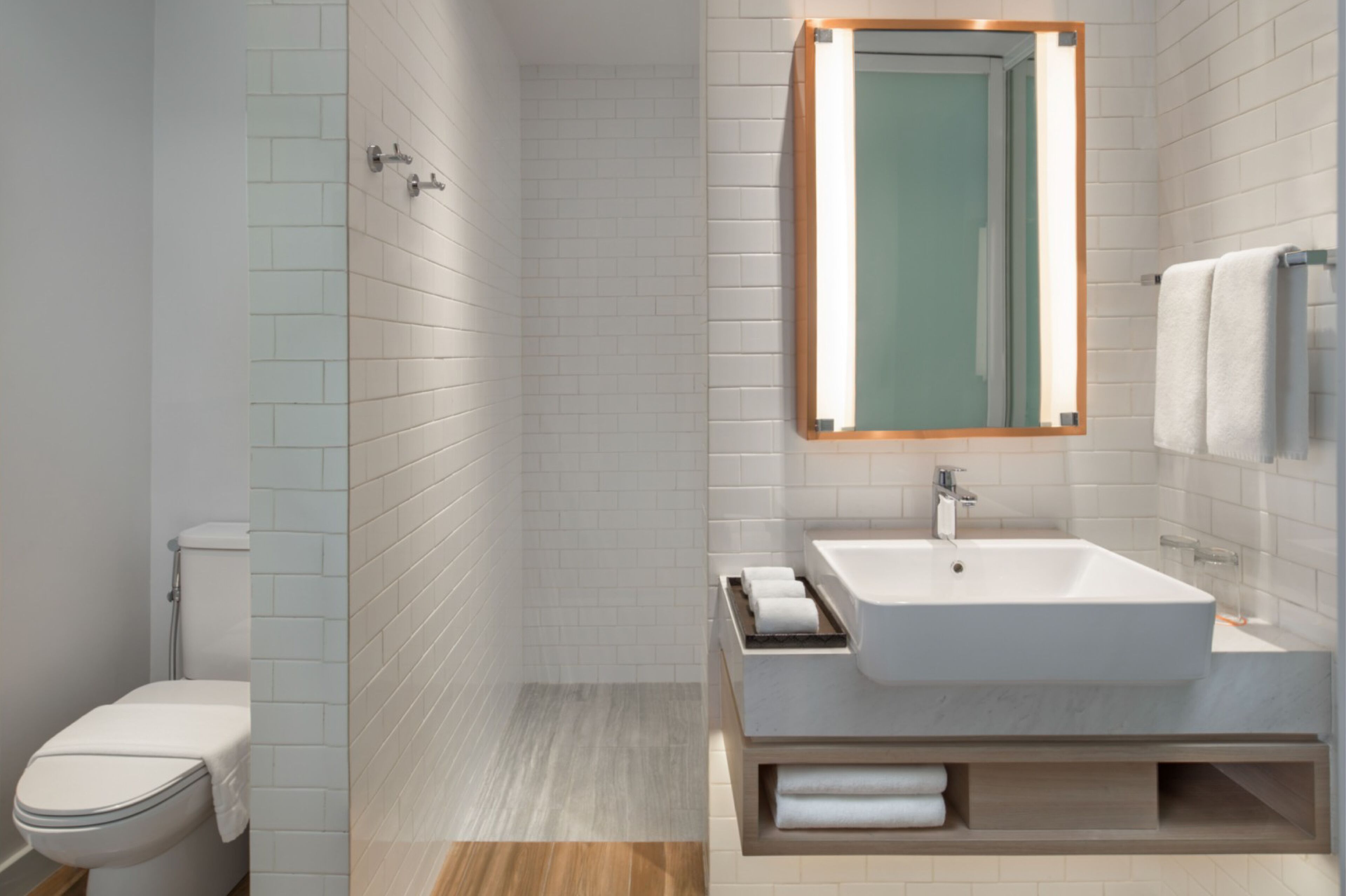 A modern bathroom with a white toilet, a large sink with a mirror, and a towel rack.
