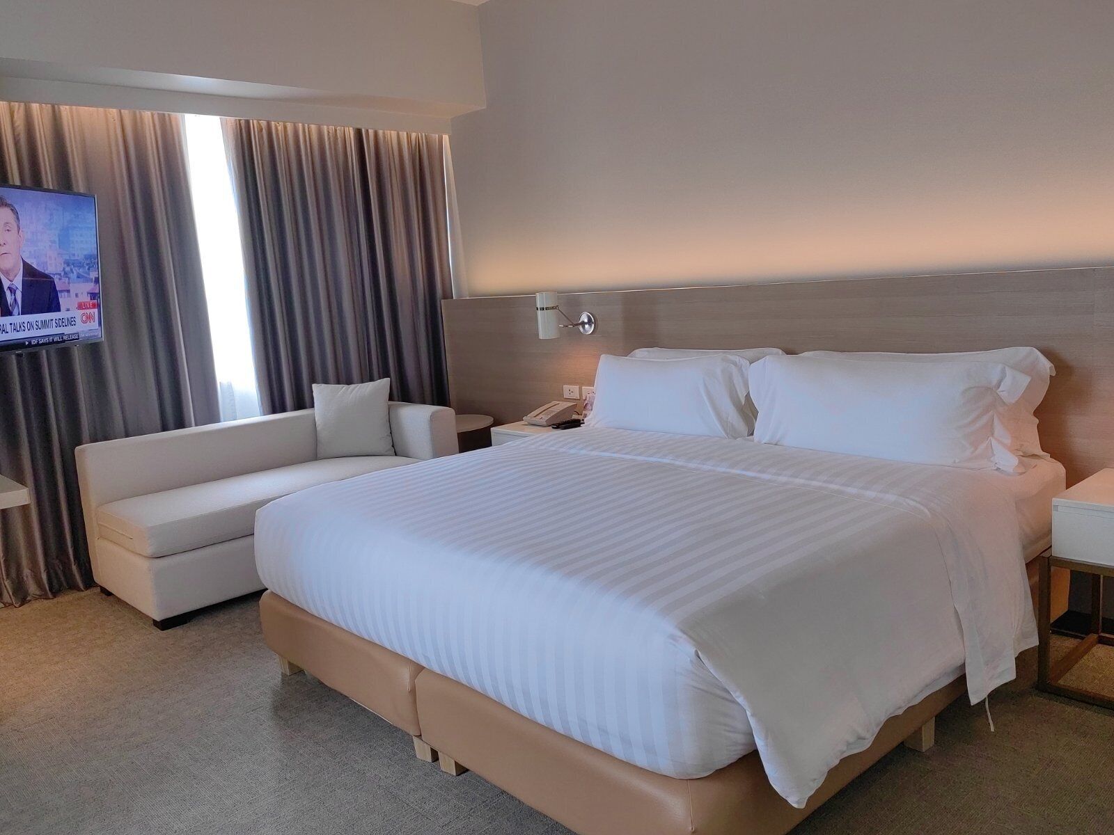 A hotel room with a large bed, a sofa, a TV, and a nightstand.