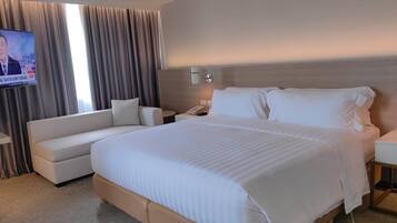 A hotel room with a large bed, a sofa, a TV, and a nightstand.