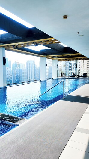 An indoor swimming pool with a city view, a sunroof, and a poolside lounge area. - Brittany Hotel BGC (Taguig)