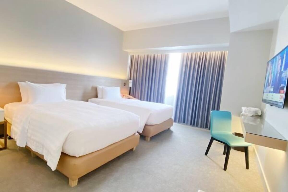 Habitación de hotel con dos camas, un escritorio, una silla y un televisor.