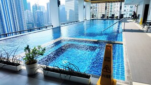 Piscina interior con vistas a la ciudad, plantas en macetas y señal de precaución por suelo mojado.