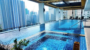 An indoor infinity pool with a city view, surrounded by potted plants, and a caution sign. - Brittany Hotel BGC (Taguig)
