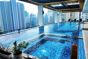 An indoor infinity pool with a city view, surrounded by potted plants, and a caution sign. - Brittany Hotel BGC (Taguig)