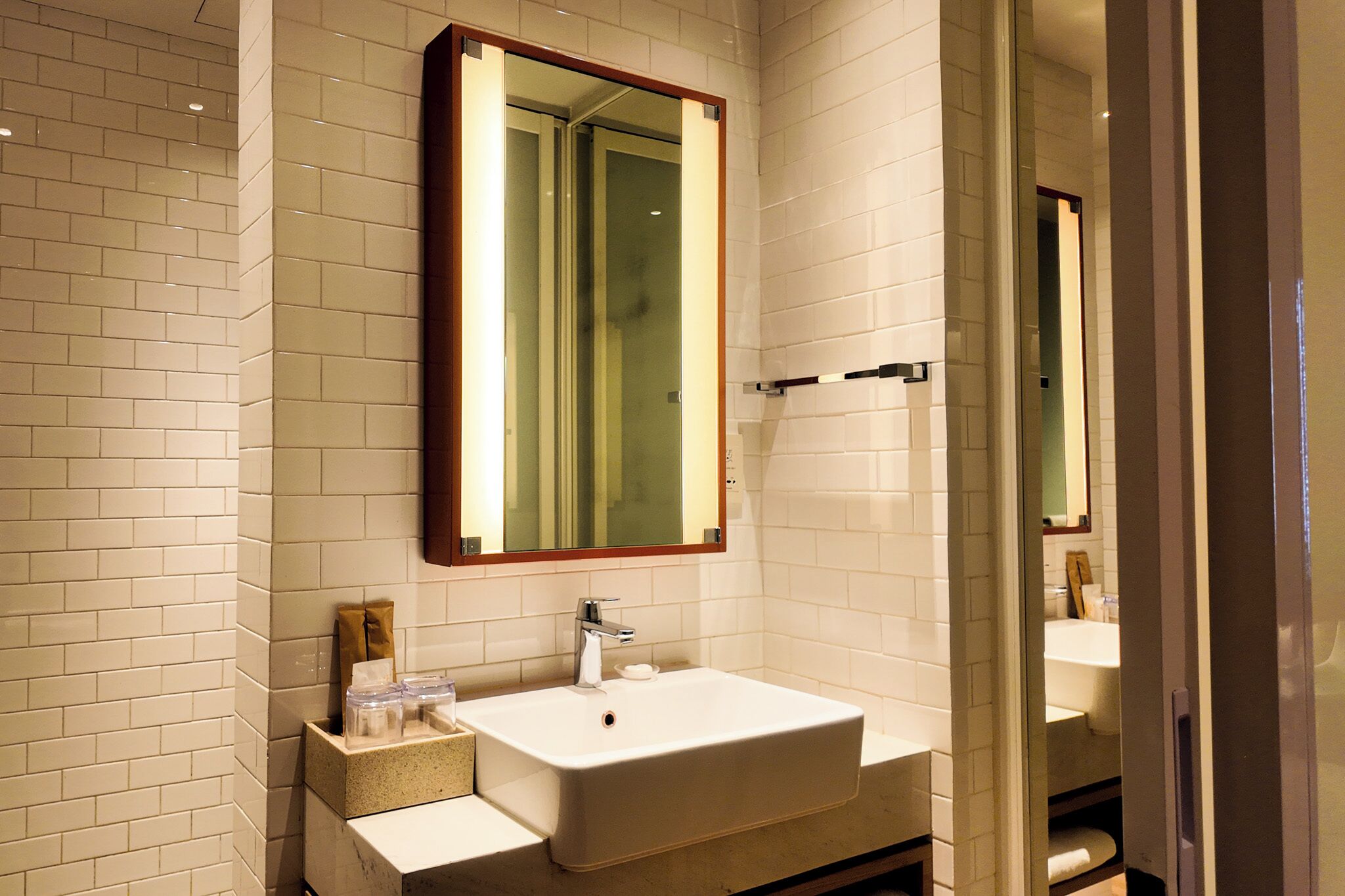 A bathroom with white tiled walls, a large mirror, a white sink, and a towel rack.