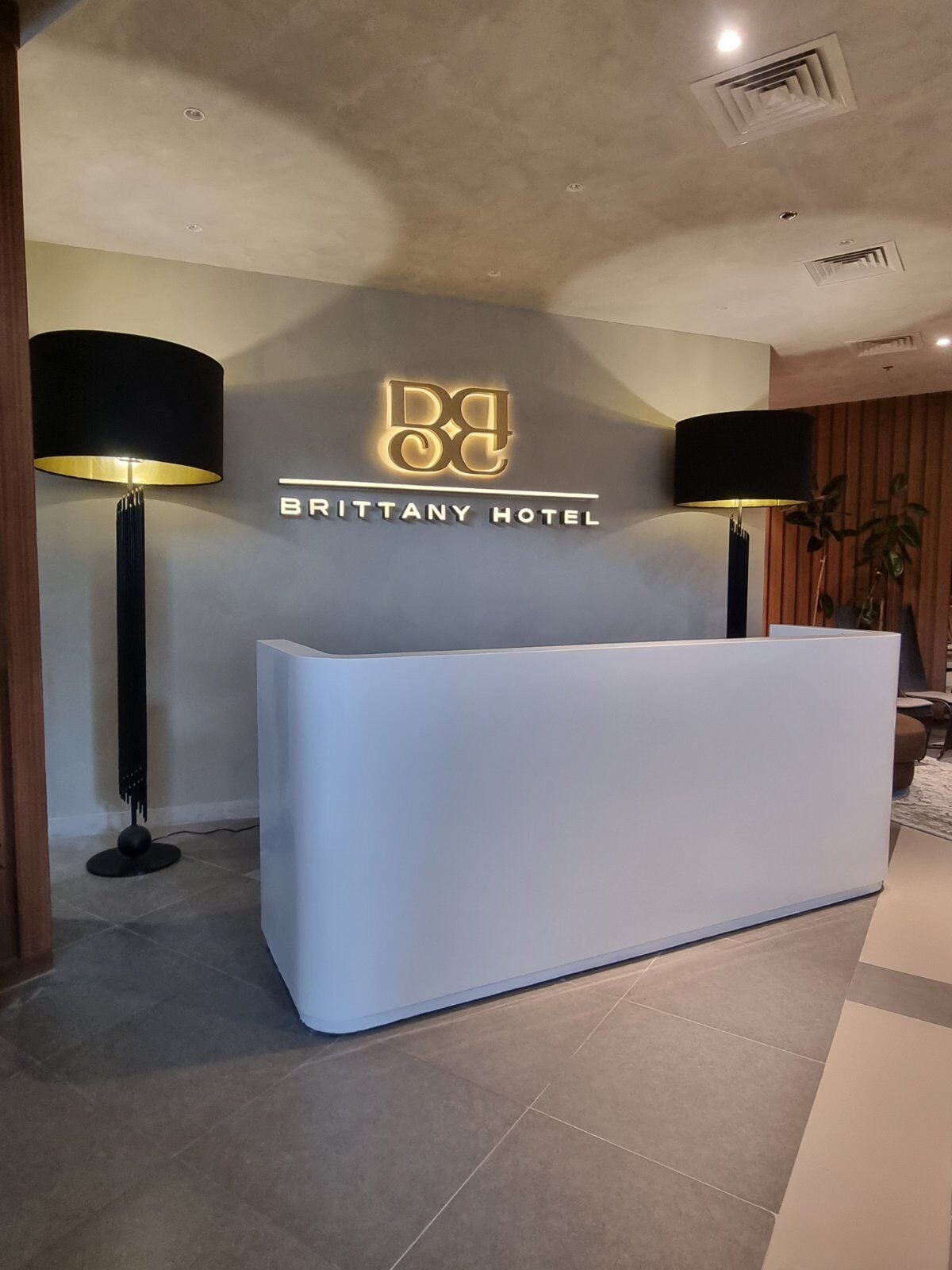 A reception desk at the Brittany Hotel with a modern design, two standing lamps, and a logo above the desk.