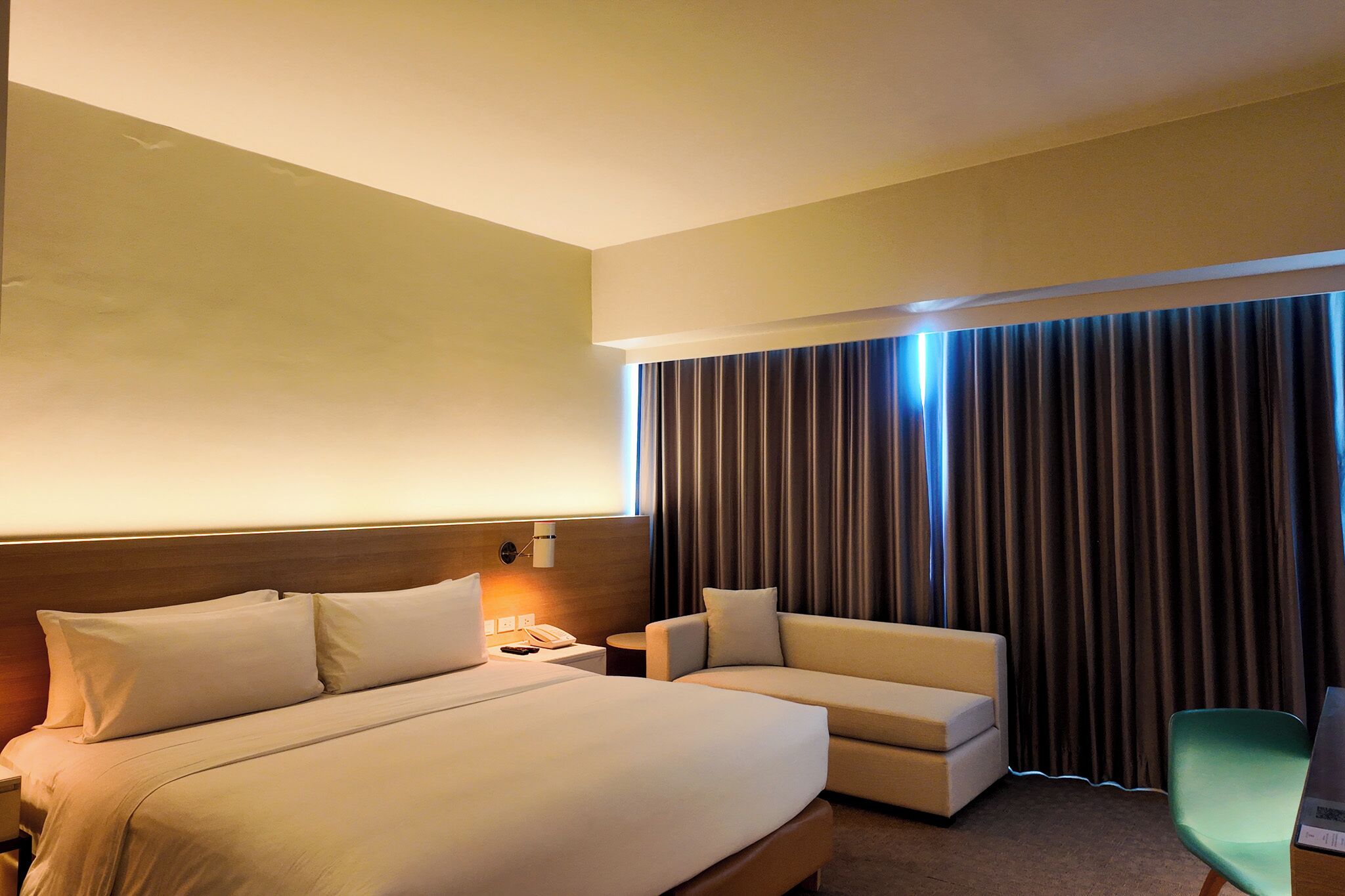 A hotel room with a large bed, a sofa, a desk with a lamp, and a curtain.