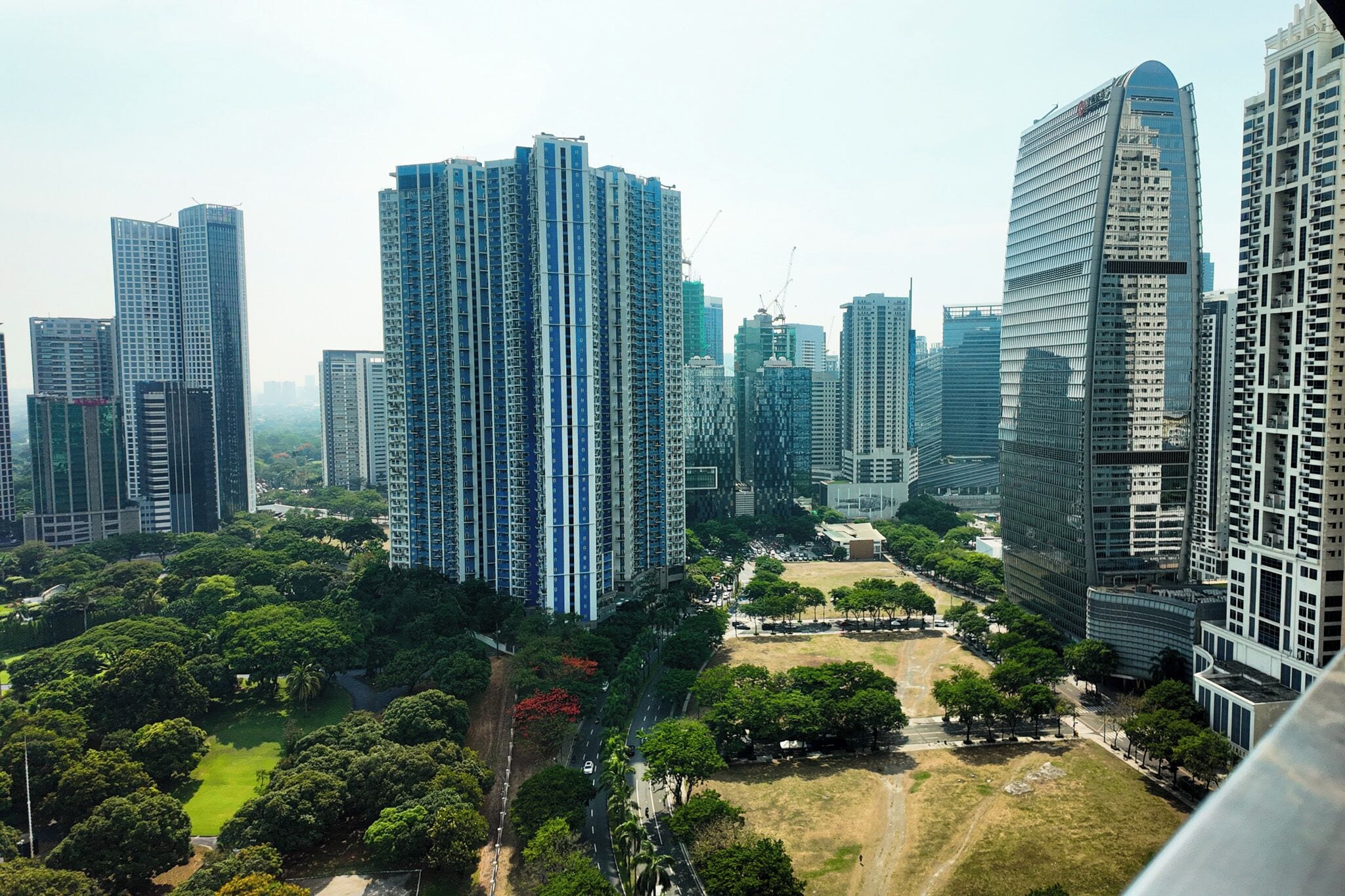 Un quartier urbain dense, avec de grands immeubles modernes, un parc central et une route.