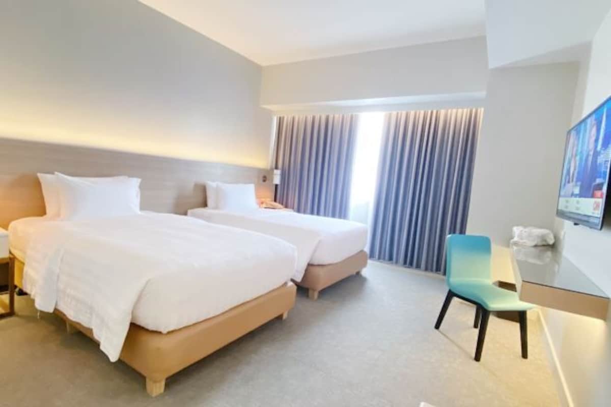 A hotel room with two beds, a desk, a chair, and a TV.