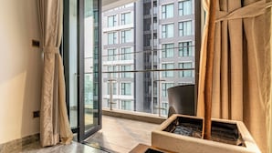 A modern hotel room with a large window, a view of a high-rise building, and a small wooden table. - 3BR APT D1Mension (Ho Chi Minh City)