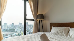A hotel room with a large bed, a view of a cityscape, and a floor lamp. - 3BR APT D1Mension (Ho Chi Minh City)