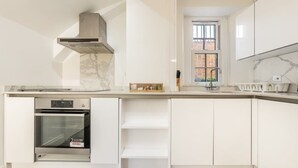 Una cocina moderna con armarios blancos, horno integrado y ventana con vista a un edificio de ladrillo.