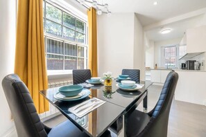 Un espace repas moderne avec une table en verre, des chaises noires et une vue sur la cuisine en arrière-plan.