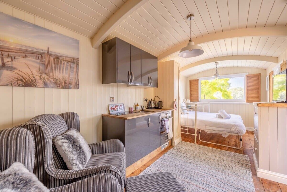Una habitación acogedora con un sofá a rayas, una pequeña kitchenette, una cama y un cuadro de una escena de playa.