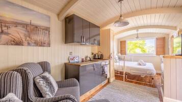Una habitación acogedora con un sofá a rayas, una pequeña kitchenette, una cama y un cuadro de una escena de playa.