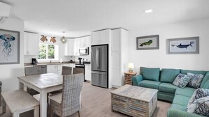 A modern kitchen with white cabinets, a stainless steel refrigerator, and a dining area with wicker chairs and a wooden table. - Oceanfront Getaway in Marathon! (Marathon)