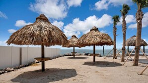A beach with thatched umbrellas and palm trees.