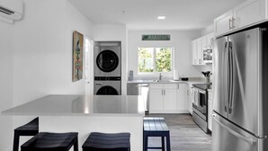 A modern kitchen with stainless steel appliances, a built-in washer and dryer, a large window, and a minimalist design.