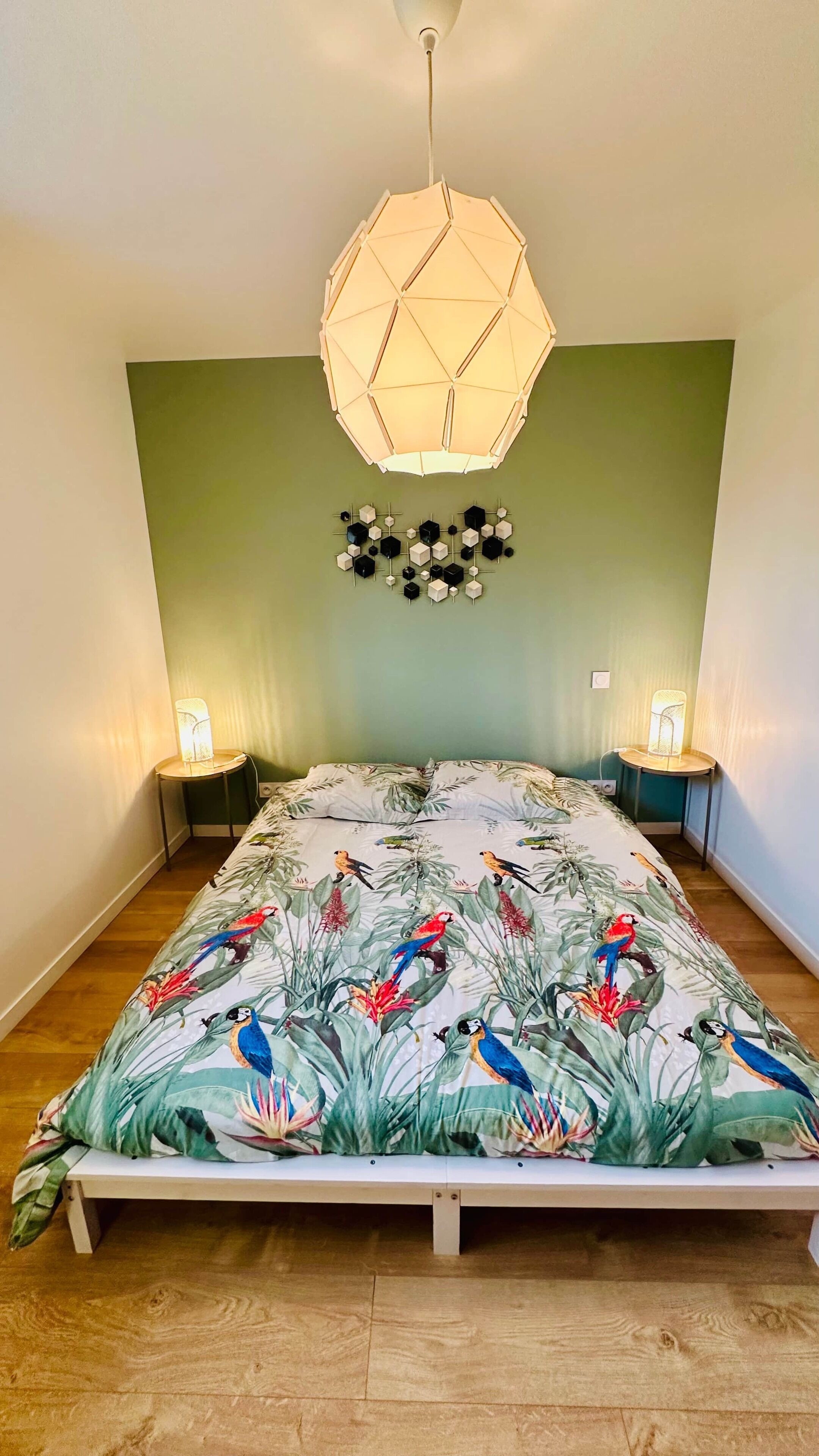 Un dormitorio con cama, dos lámparas de noche, una lámpara de techo geométrica y un adorno en la pared.