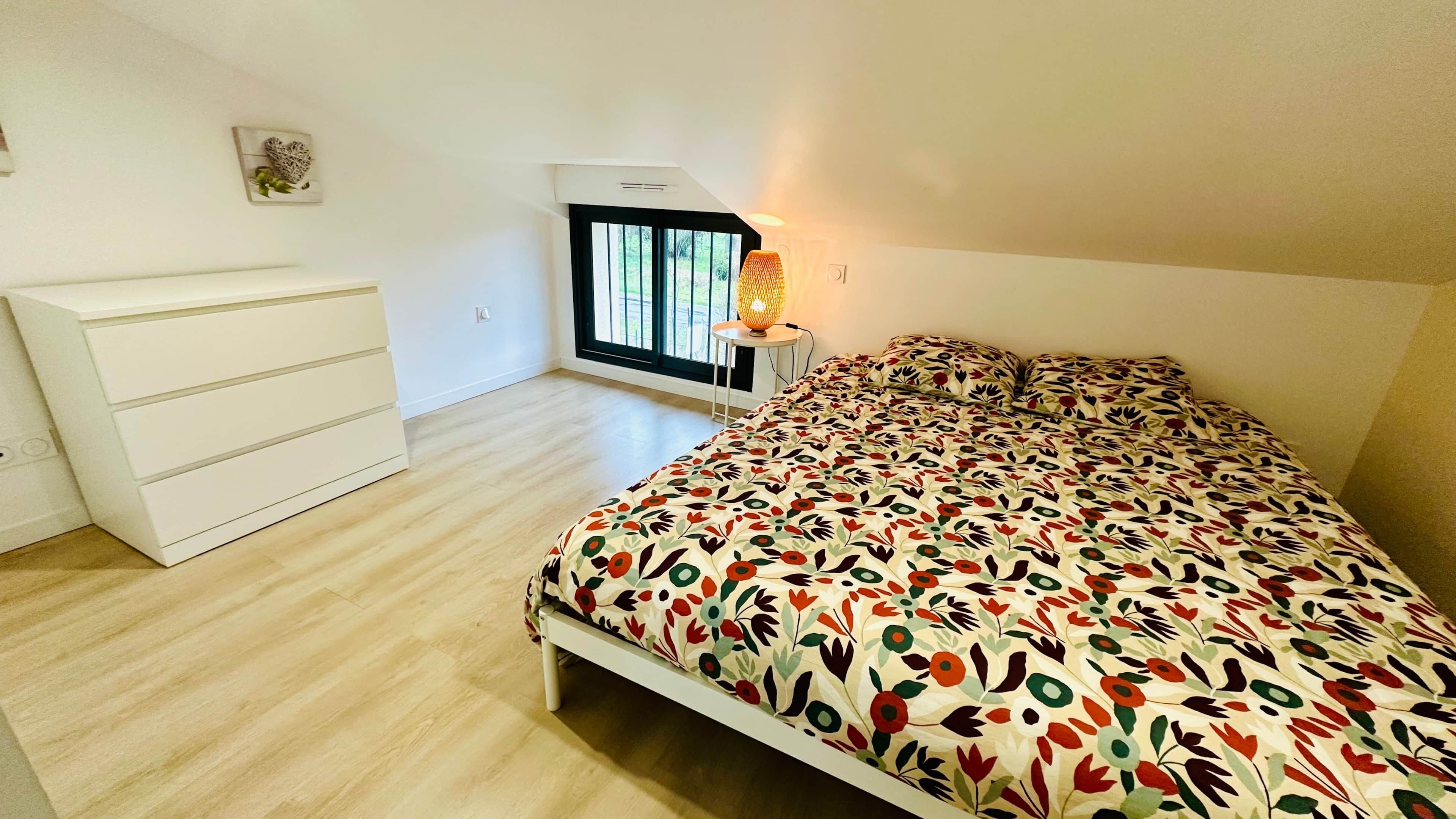 Un dormitorio con cama, cómoda, ventana y lámpara.
