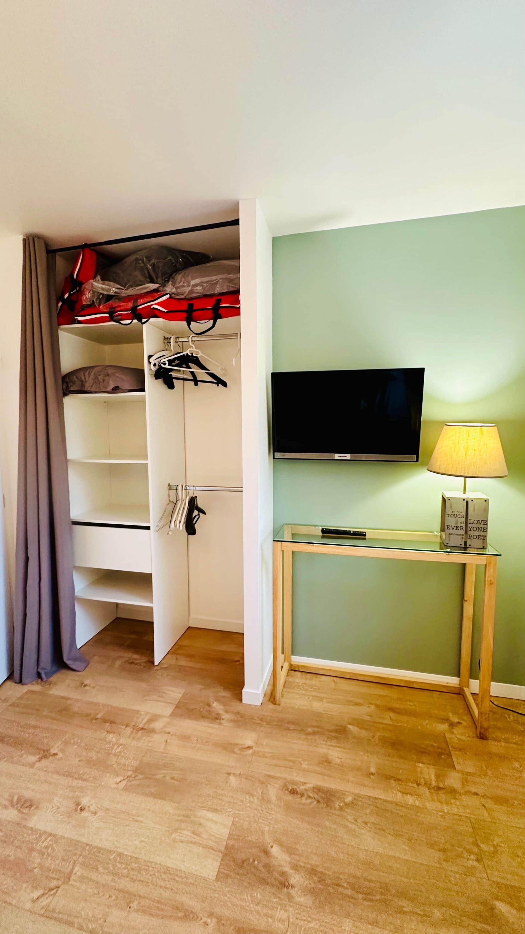 Habitación pequeña con una cama individual superpuesta, televisión, una mesita con lámpara y suelo de madera.