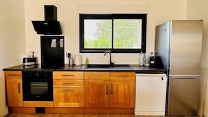 A compact kitchen with a built-in oven, a dishwasher, a black range hood, a stainless steel refrigerator, and a window above the sink. - Le Grand *** - 3 bedrooms, all new & all inclusive (Montauban)