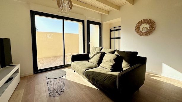 A modern living room with a sofa, a TV, and a large sliding glass door leading to a balcony. - Le Grand *** - 3 bedrooms, all new & all inclusive (Montauban)
