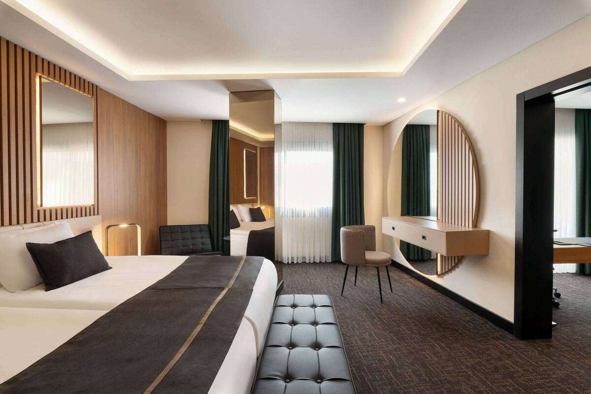 Une chambre d’hôtel moderne dotée d’un grand lit, d’un coin salon, d’un bureau et d’un grand miroir.