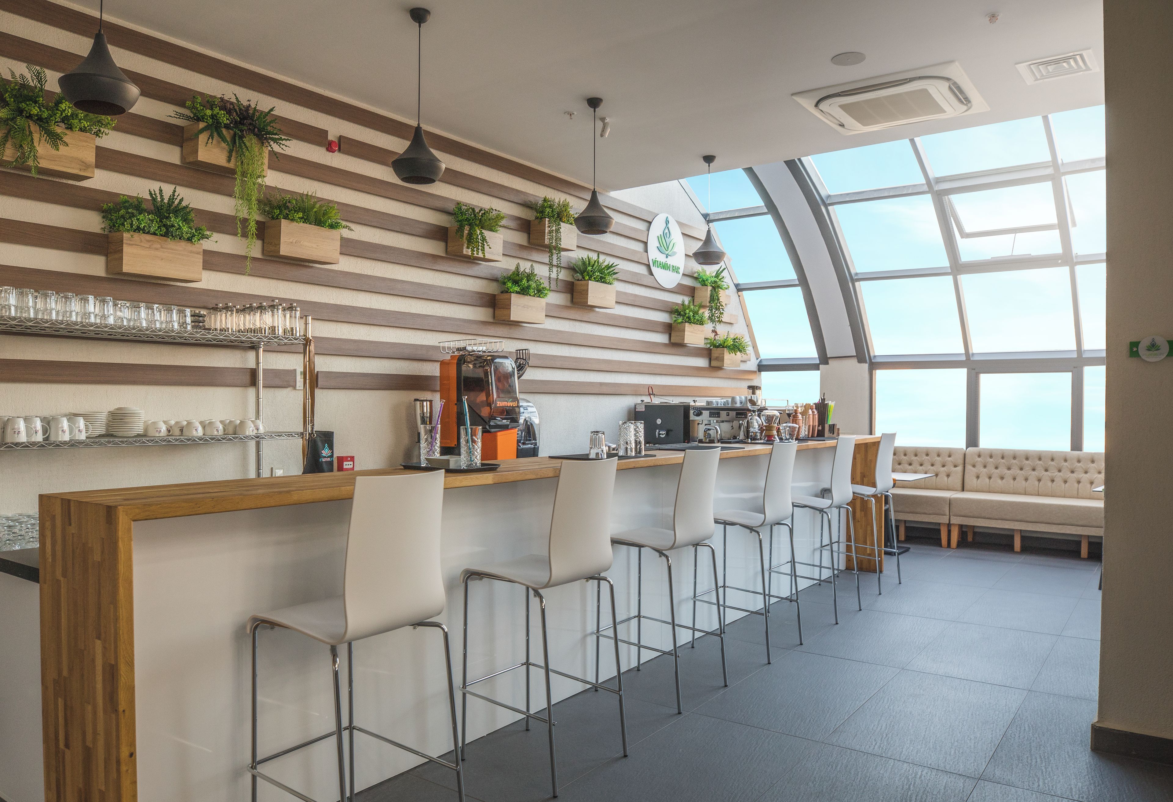 Zona de bar moderna con mostrador de madera, taburetes y un área de estar con sofá.