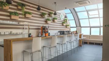 Zona de bar moderna con mostrador de madera, taburetes y un área de estar con sofá.