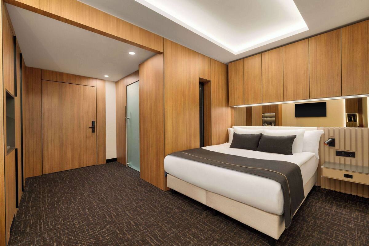 Une chambre d’hôtel moderne dotée d’un grand lit, de lambris en bois, d’un téléviseur à écran plat et d’une table de chevet.