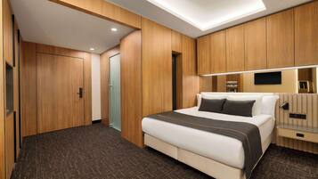 Una habitación de hotel moderna con una cama grande, paneles de madera, un televisor de pantalla plana y una mesita de noche.