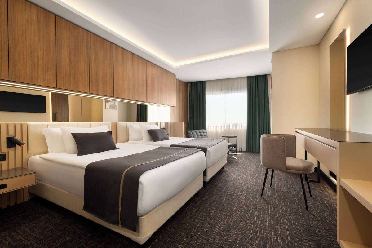 Une chambre d’hôtel avec deux lits, un bureau, une chaise, une télévision et une fenêtre avec des rideaux.