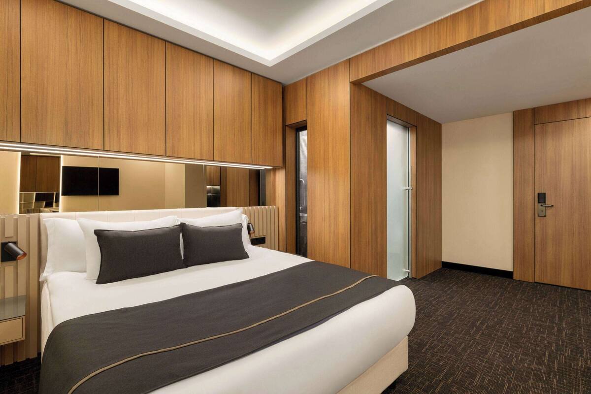 Une chambre d’hôtel avec un grand lit, des boiseries, un téléviseur à écran plat et une porte donnant sur une autre pièce.