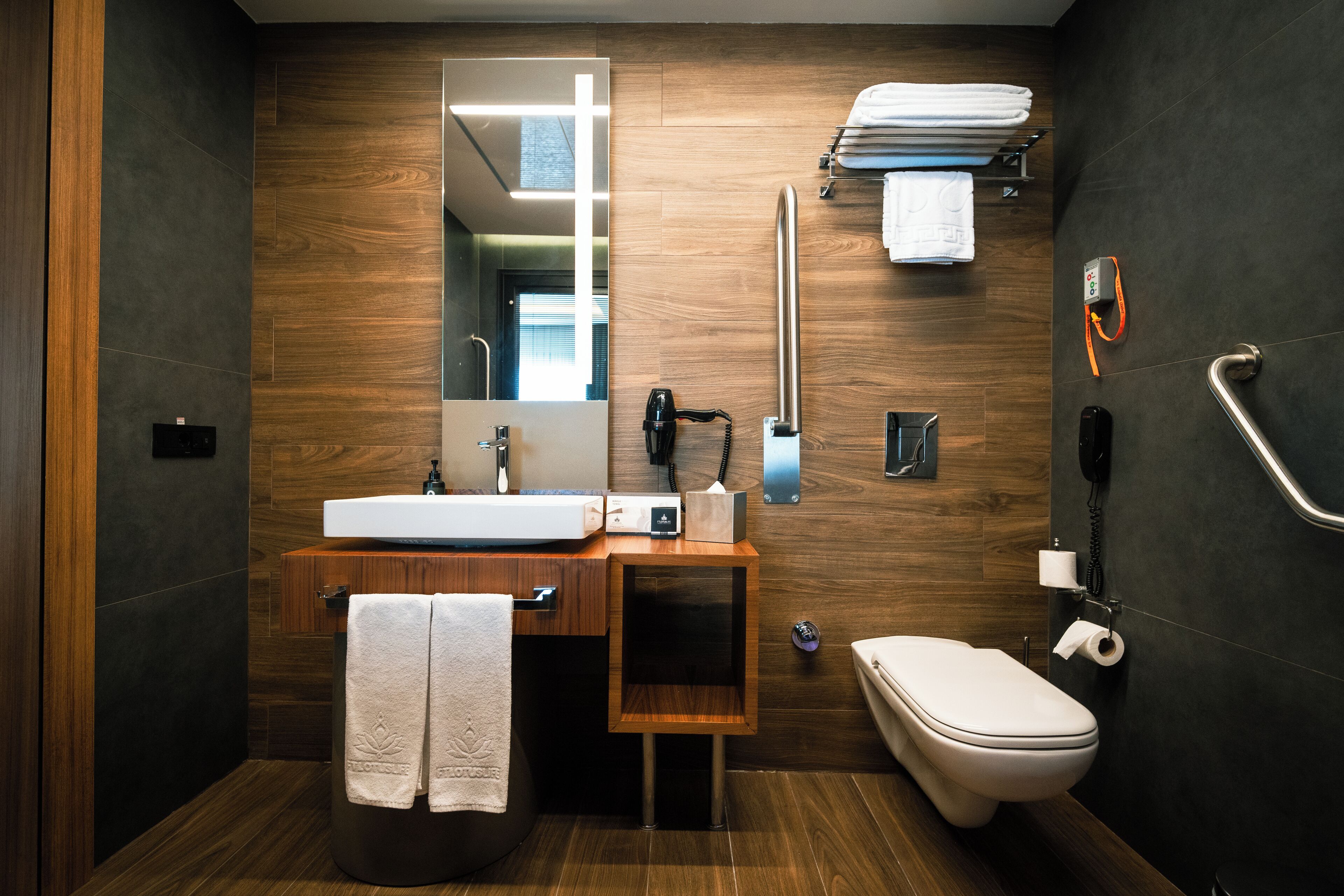 A modern bathroom with a wooden vanity, a large mirror, a toilet, and a towel rack.