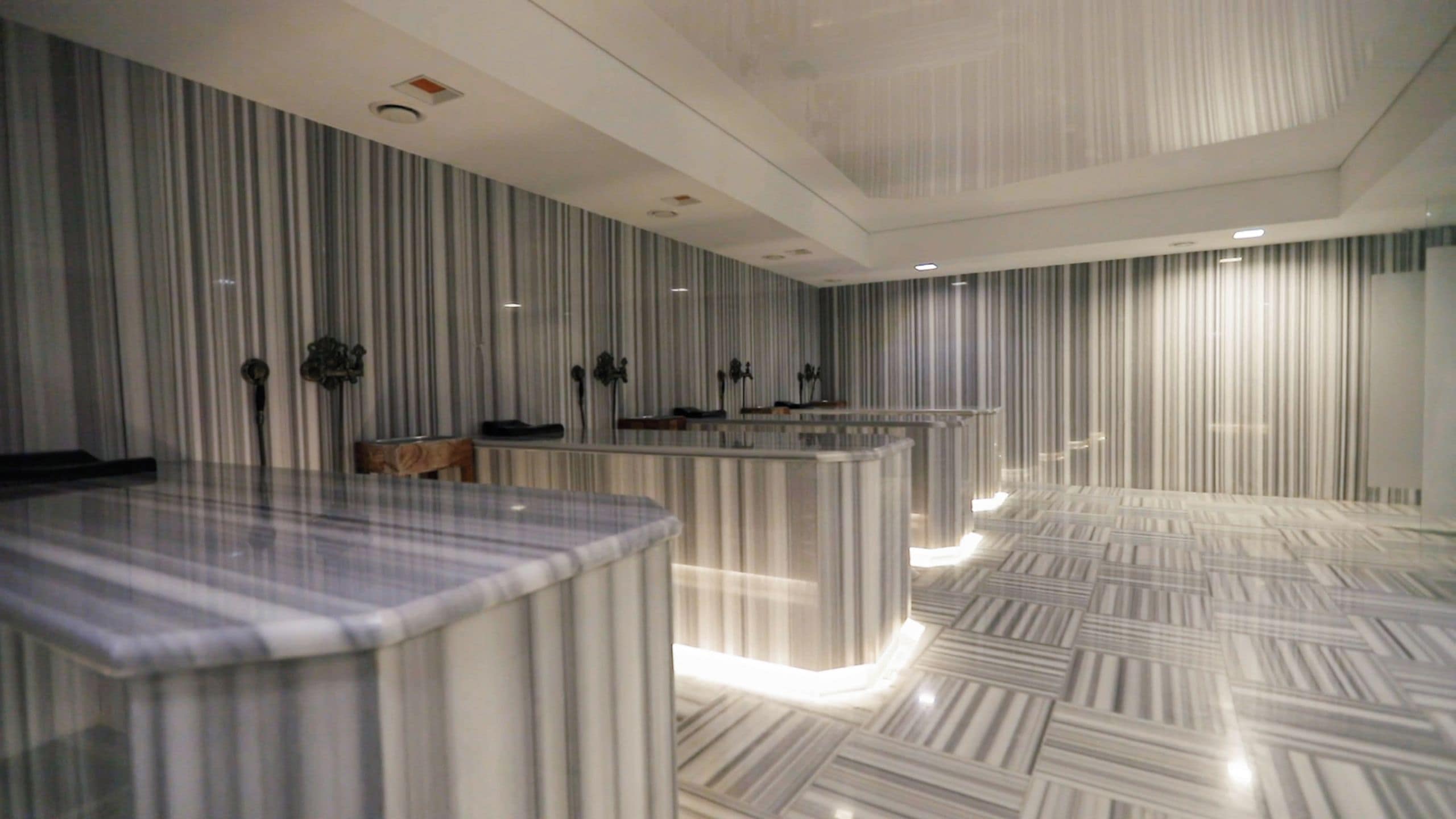 A modern hotel lobby with a marble reception desk, a seating area, and a patterned floor.