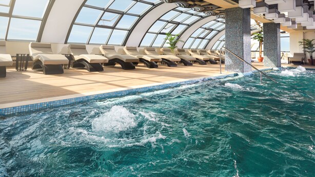 Ein moderner Poolbereich im Innenbereich mit Liegestühlen und einer großen, klaren Glaskuppel.