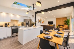 A modern kitchen with a central island, stainless steel appliances, and a dining area with a wooden table set for six.