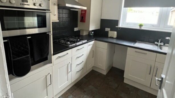 A kitchen with white cabinets, a black stove, and a window with a view. - The Heilan` Coo Apartment (Argyll and Bute Council)