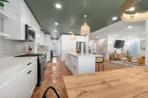 A modern kitchen with white cabinets, a large island, and a dining area with wooden furniture. - SoCo BoHo Bungalow | Main House (Austin)