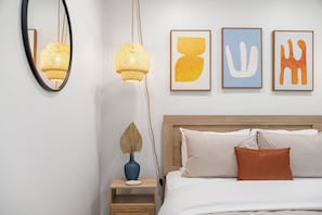A bedroom with a wooden headboard, a white bed, and three framed abstract paintings on the wall.