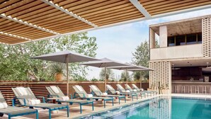 A poolside area with lounge chairs and umbrellas, a clear pool, and a modern building structure in the background. - SoCo BoHo Bungalow | Main House (Austin)