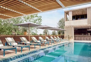 Ein Poolbereich mit Liegestühlen und Sonnenschirmen, ein klares Schwimmbecken und ein modernes Gebäude im Hintergrund.