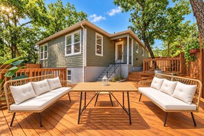 A house with a deck, two wicker sofas, a table, and a staircase leading to the entrance. - SoCo BoHo Bungalow | Main House (Austin)