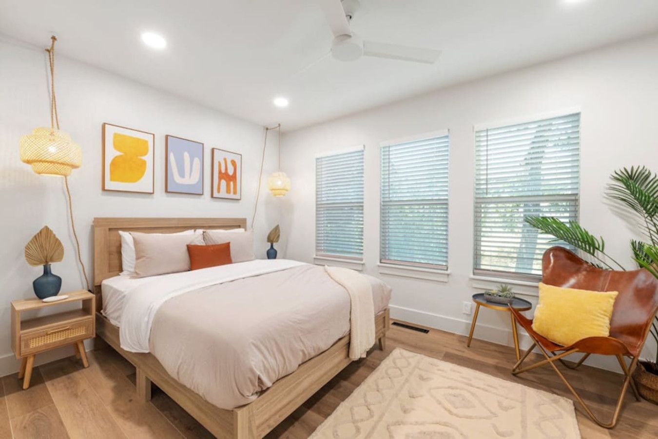 A modern bedroom with a wooden bed, a small side table, a chair, and a large window with blinds.